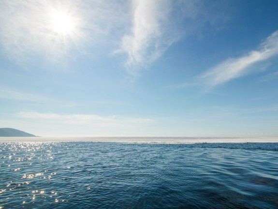 Wide angle view of the sea with sun reflections and blue sky with light veil clouds	